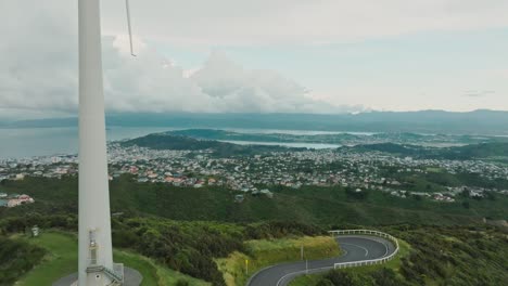 Aerial-view-rising-above-Brooklyn-wind-turbine-with-scenic-landscape-views-of-capital-city-Wellington,-harbour-and-hills,-in-North-Island-of-New-Zealand-Aotearoa