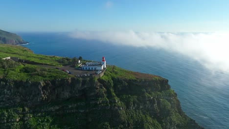 Drone-push-in-to-lighthouse-looking-out-on-blue-ocean-with-misty-sunlit-clouds-on-horizon