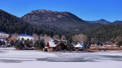 First-snow-ice-frozen-covered-white-Evergreen-Lake-House-Rocky-Mountain-landscape-scene-morning-front-range-Denver-aerial-cinematic-drone-Christmas-ice-skating-hockey-blue-sky-circle-left-motion