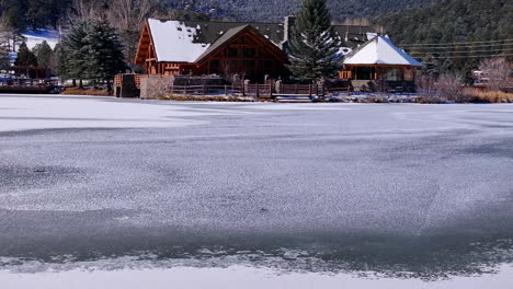 First-snow-ice-frozen-covered-white-Evergreen-Lake-House-Rocky-Mountain-landscape-scene-morning-front-range-Denver-aerial-cinematic-drone-Christmas-ice-skating-hockey-blue-sky-pan-up-forward-motion