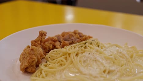 Pieces-of-fried-chicken-served-with-spaghetti-with-white-sauce-and-some-spices,-looks-like-a-delicious-Carbonara-meal