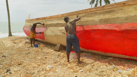 black-male-fisherman-painting-his-fisherman-boat-in-tropical-beach-doing-maintenance-Job