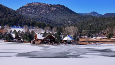 First-snow-ice-frozen-covered-white-Evergreen-Lake-House-Rocky-Mountain-landscape-scene-morning-front-range-Denver-aerial-cinematic-drone-Christmas-ice-skating-hockey-blue-sky-right-motion