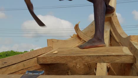 Hombre-Negro-Descalzo-Tallando-Y-Cortando-Un-Barco-De-Madera-Con-Azuela-En-Ghana