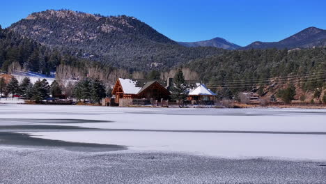 First-snow-ice-frozen-covered-white-Evergreen-Lake-House-Rocky-Mountain-landscape-scene-morning-front-range-Denver-aerial-cinematic-drone-Christmas-ice-skating-hockey-blue-sky-slow-to-right-motion