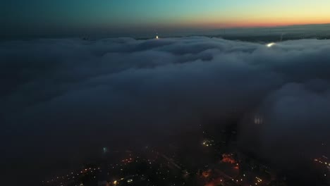 Aerial-birds-eye-shot-over-dark-cloudscape-and-illuminated-city-on-the-valley-at-sunrise-time