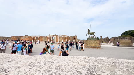 Visitors-explore-the-ancient-ruins-of-Pompeii,-with-the-renowned-centaur-statue-standing-prominently-in-the-background