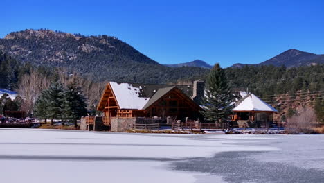 First-snow-ice-frozen-covered-white-Evergreen-Lake-House-Rocky-Mountain-landscape-scene-front-range-Denver-aerial-cinematic-drone-Christmas-ice-skating-hockey-bluesky-slow-slide-pan-right-motion