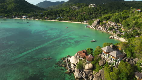 Koh-Tao-south-east-Asia-tropical-paradise-with-sand-beach-and-pristine-ocean-clear-water-sea,-drone-revealing-bay-with-beach-resort-luxury-accommodation-above-the-rocky-cliff