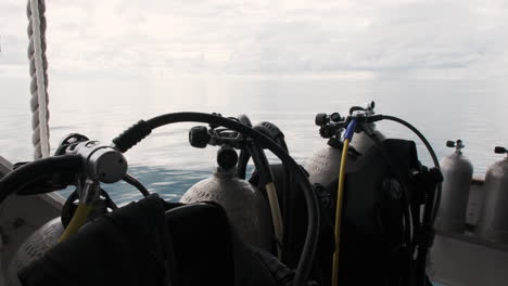 Scuba-tanks-stand-ready-on-a-boat-deck,-the-vast-ocean-and-a-cloudy-sky-stretching-out-in-the-background