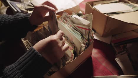 A-person’s-hands-going-through-a-box-of-old-letters-and-postcards-stacked-haphazardly-in-a-box