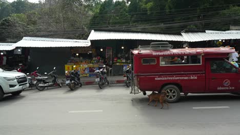 Furgoneta-Roja-Pasando-Por-Tiendas-Locales-Y-Motocicletas-En-Una-Calle-Muy-Transitada-De-La-Ciudad-De-Chiang-Mai,-Tailandia