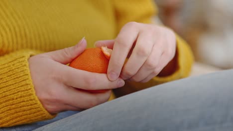 Young-woman-peeling-orange-or-mandarin-white-sitting,-cozy-homescape
