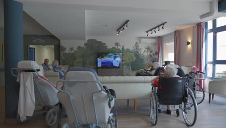 Gruppe-älterer-Frauen-Im-Rollstuhl-Vor-Dem-Fernseher-In-Einem-Altenpflegezentrum