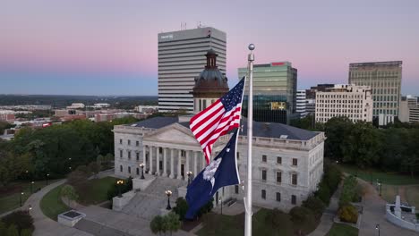 South-Carolina-State-House-Mit-Amerikanischen-Und-Sc-Flaggen,-Die-Bei-Sonnenaufgang-Vor-Der-Skyline-Von-Columbia-Wehen