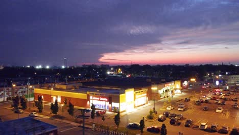 Drone-flies-above-strip-mall-parking-lot-with-epic-curved-clouds-hosting-red-pink-sunset-hues-in-sky