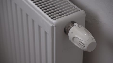 Reducing-radiator-or-heating-thermostat-temperature,-hand-closeup,-saving-money-during-economic-crisis