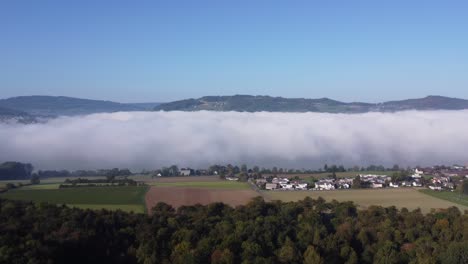 Drohnenaufnahme-Von-Dichtem-Nebel,-Der-Den-See-Bedeckt-Und-Wie-Wolken-Auf-Dem-Boden-Aussieht