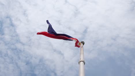 Bandera-Ondeando-A-La-Izquierda-Mientras-Los-Pájaros-Vuelan-Sobre-Ella-Y-Nubes-Parecidas-Al-Algodón-Como-Fondo,-Capturadas-Desde-Debajo-Del-Asta-De-La-Bandera-Nacional-De-Filipinas