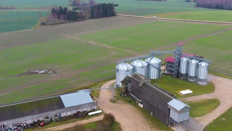 Modern-grain-silos-in-huge-farm-surrounded-with-agriculture-fields,-aerial-view