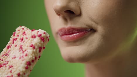 Close-up-shot-of-a-young-woman-enjoying-a-delicious-vegan-ice-cream-with-vanilla-and-strawberry-flavor-in-front-of-green-background-in-slow-motion