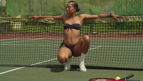 Enjoying-the-sunshine,-a-young-African-girl-exhibits-her-tennis-prowess-in-a-trendy-bikini-whike-squating-low-angle