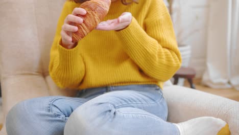 Casual-woman-eats-delicious-croissant-on-couch,-front-view