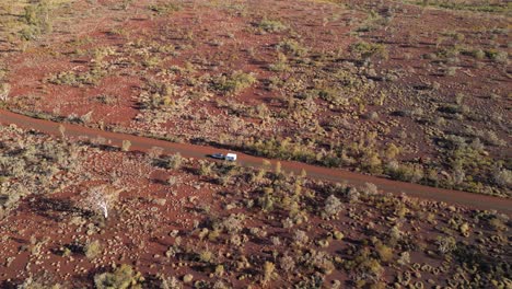 Aerial-tracking-shot-of-Camper-Van-trailer-driving-on-desert-road-during-sunset-in-Karijini-National-Park,-Australia