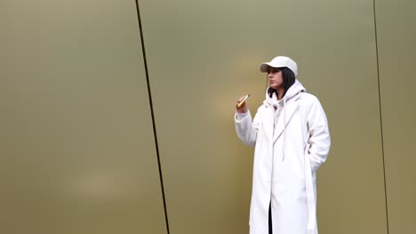 Female-in-white-coat-and-cap-smoke-electronic-cigarette-near-golden-wall