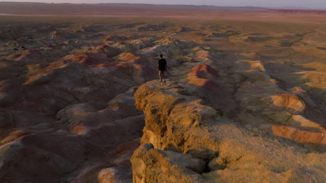 Man-On-The-Edge-Of-A-Cliff-At-Tsagaan-Suvarga-In-The-Mongolian-Gobi-Desert-At-Sunset---Drone-Pullback