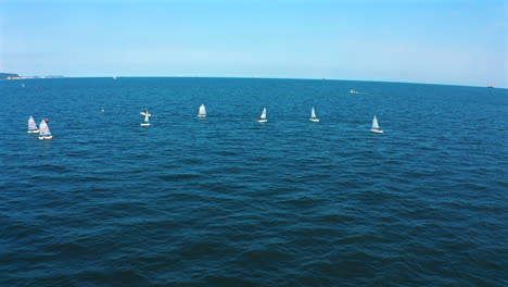 Aerial-view-of-Optimist-dinghy-boats-sailing-on-the-blue-ocean-at-sunny-day