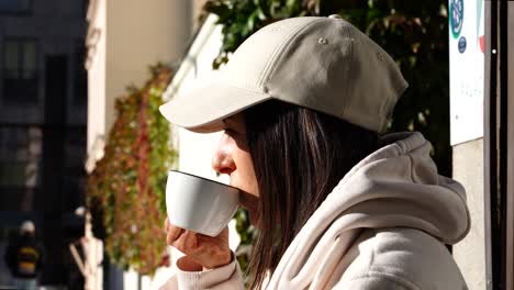 Girl-in-white-hoodie-and-cap-peacefully-drink-cup-facing-sunlight-in-cafe
