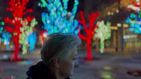 Senior-woman-walking-in-a-city-decorated-with-Christmas-lights-at-nighttime