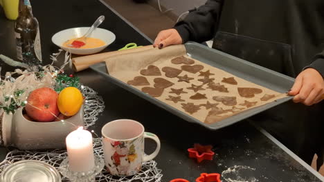 Woman-grabs-tray-with-gingerbread-cookies-cut-in-cute-shapes-ready-for-the-oven