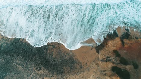 Top-view-drone-on-the-waves-hitting-a-rocky-shore-and-spreading-out