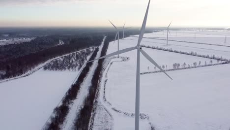 Luftaufnahme-Eines-Windkraftparks-Während-Einer-Verschneiten-Winterlandschaft-In-Der-Nähe-Des-Waldes