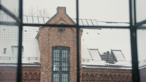 Snowflakes-drift-past-a-window,-framing-a-historic-brick-building