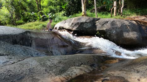 A-boy-slides-down-Mo-Pang-Waterfall-in-Pai,-Thailand