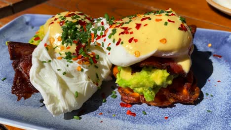 Tasty-Eggs-Benedict-breakfast-dish-with-crispy-bacon,-hollandaise-sauce-and-avocado-on-sweet-potato-hash-browns,-poached-eggs-for-brunch-at-a-restaurant,-4K-shot