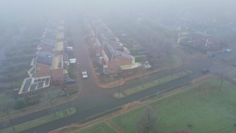 Aerial-of-car-driving-over-mist-covered-street-of-suburban-neighborhood