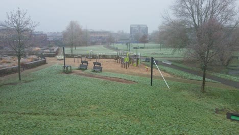Low-aerial-of-urban-basketbal-court-towards-a-children-playground-on-a-cold-and-misty-morning