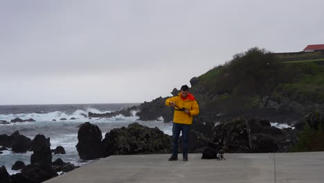 Man-setting-up-tripod-on-rocky-coast-with-waves-of-Atlantic-Ocean-shore-in-Terceira,-Azores
