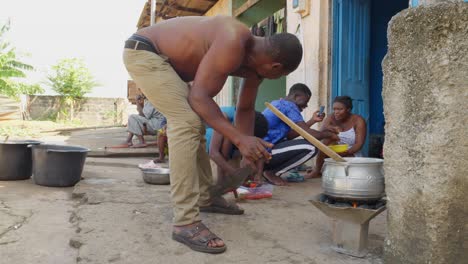 Man-stirs-the-fire-of-the-pot-where-Banku,-mixture-of-maize-and-cassava,-Ghanaian-cuisine,-is-cooked
