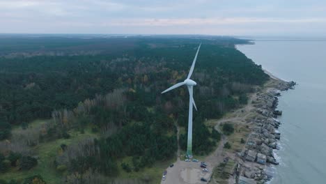 Establishing-aerial-view-of-abandoned-seaside-fortification-buildings-at-Karosta-Northern-Forts-on-the-beach-of-Baltic-sea-in-Liepaja,-overcast-day,-wind-turbine,-drone-shot-moving-forward