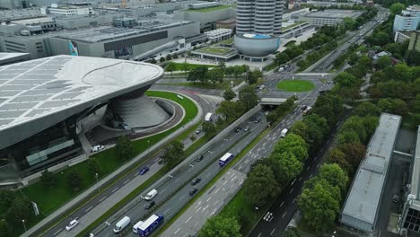 Aerial-reveal,-BMW-Museum,-the-city-roads-surrounding-and-buildings-beyond