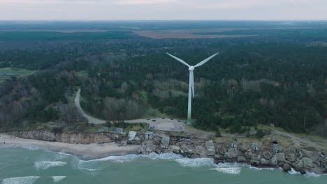 Establishing-aerial-view-of-abandoned-seaside-fortification-buildings-at-Karosta-Northern-Forts-on-the-beach-of-Baltic-sea-in-Liepaja,-overcast-day,-wind-turbine,-drone-shot-moving-forward,-tilt-down