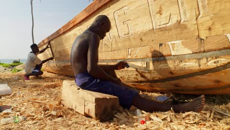 Black-african-carpenters-smoothing-and-chiseling-hull-of-wooden-boat