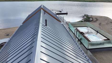 flying-over-the-tin-roof-of-a-lakehouse-revealing-a-boat-dock-on-the-lake-and-moody-mountain-terrain-AERIAL-DOLLY-TILT