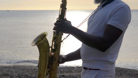 Músico-Africano-Senior-Tocando-El-Saxofón-En-Una-Playa-Durante-La-Puesta-De-Sol
