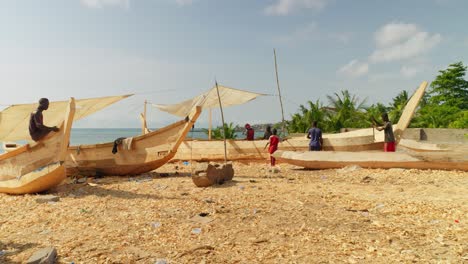 Black-african-carpenters-working-on-new-wooden-boats-on-beach,-Ghana